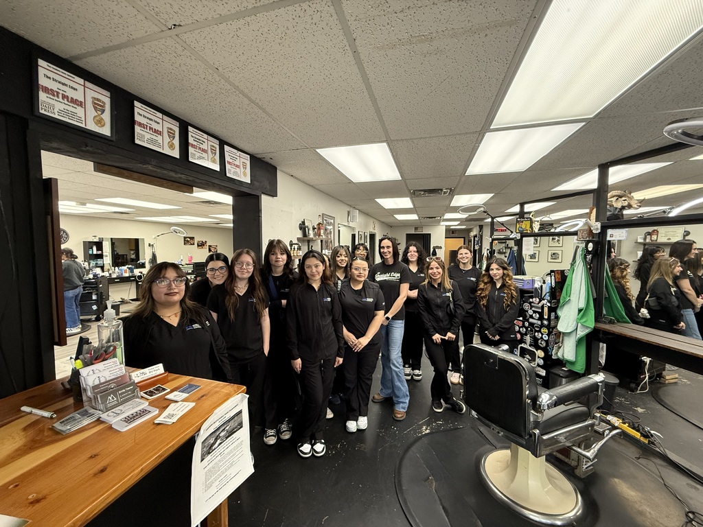 A group of women in black uniforms standing in a salon with chairs, a table, and mirrors.