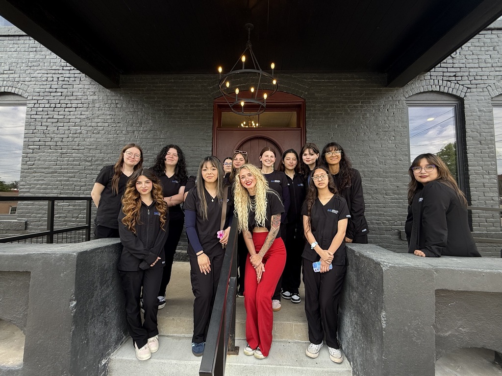 A group of women in black uniforms stand on steps in front of a gray building with glass windows.
