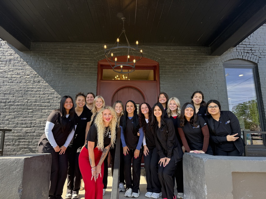 A group of women in black uniforms stands on a porch. A brick wall, a door, and a chandelier are in the background.