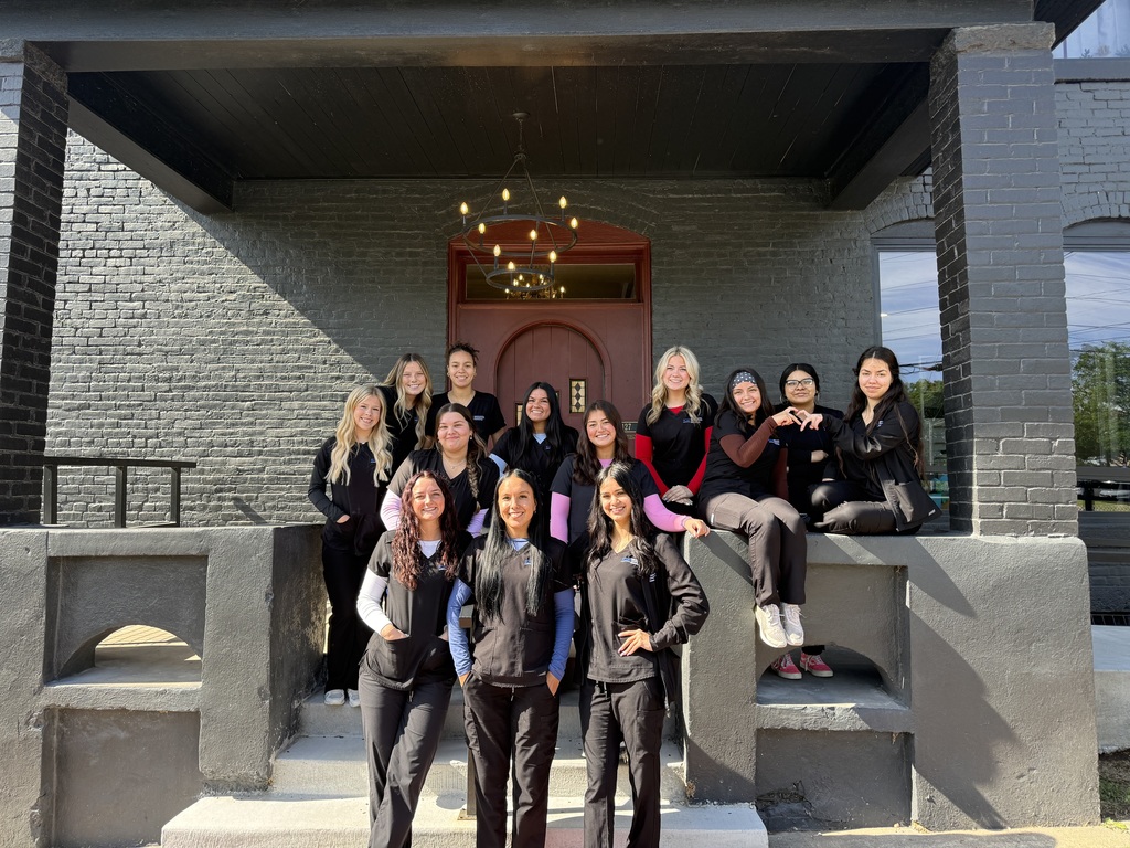A group of women dressed in matching black outfits pose for a photo outside a building.