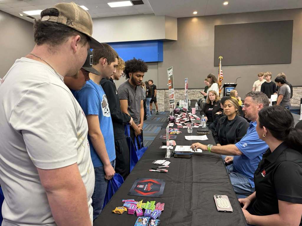 A group of people are gathered around a table covered in colorful game pieces and papers.