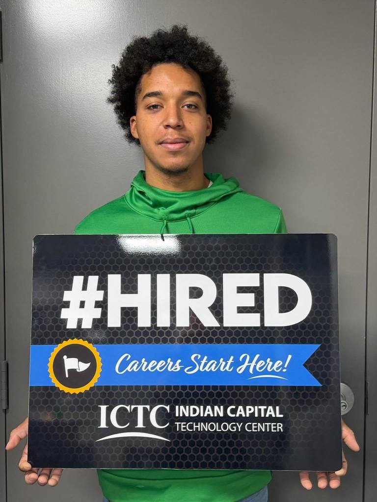 A person in a green shirt holds a sign that says "#HIRED Careers Start Here!" in front of a gray background.