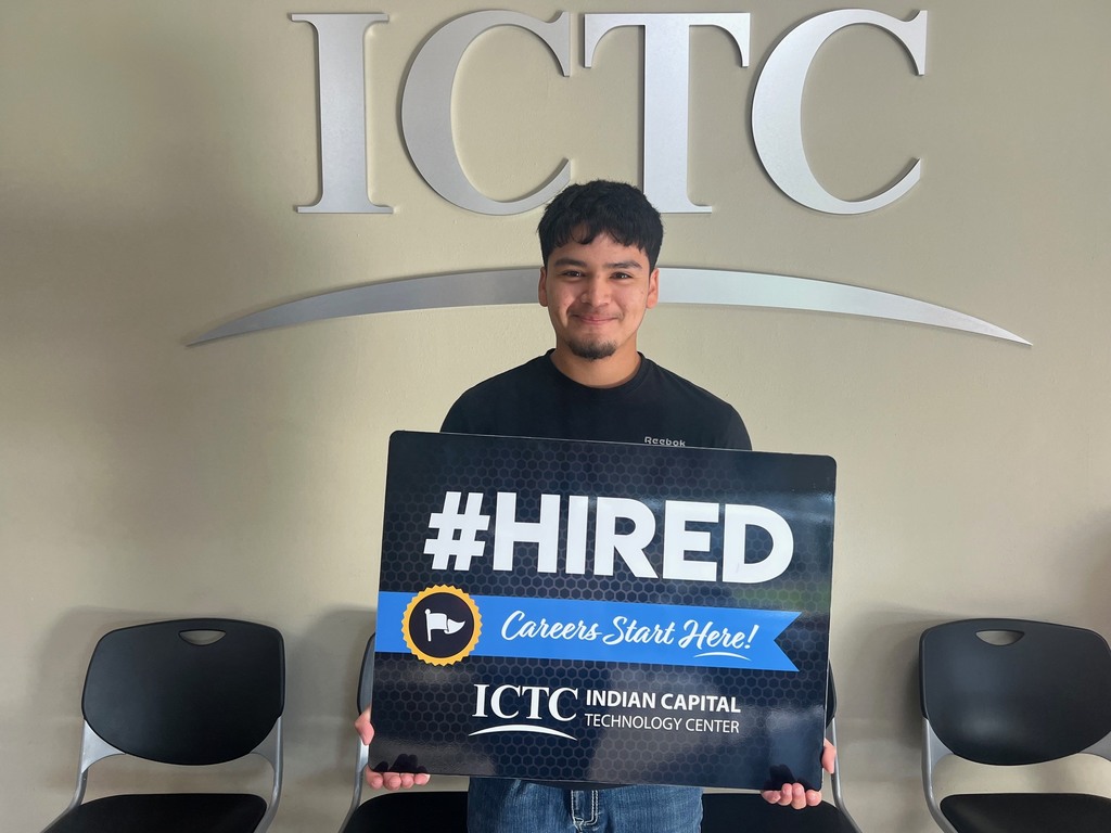 Person holds a sign that reads "#HIRED" in front of the ICTC logo and two empty chairs.
