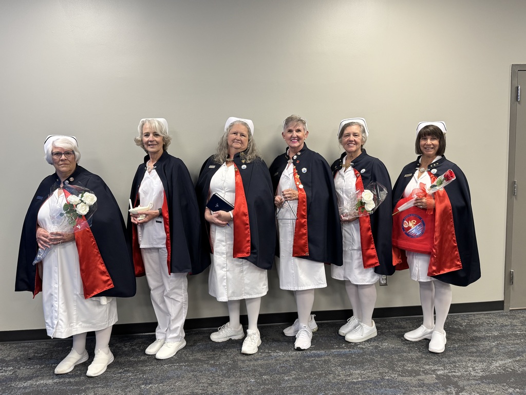 A group of women dressed in matching white uniforms, capes, and white shoes stand in a row.