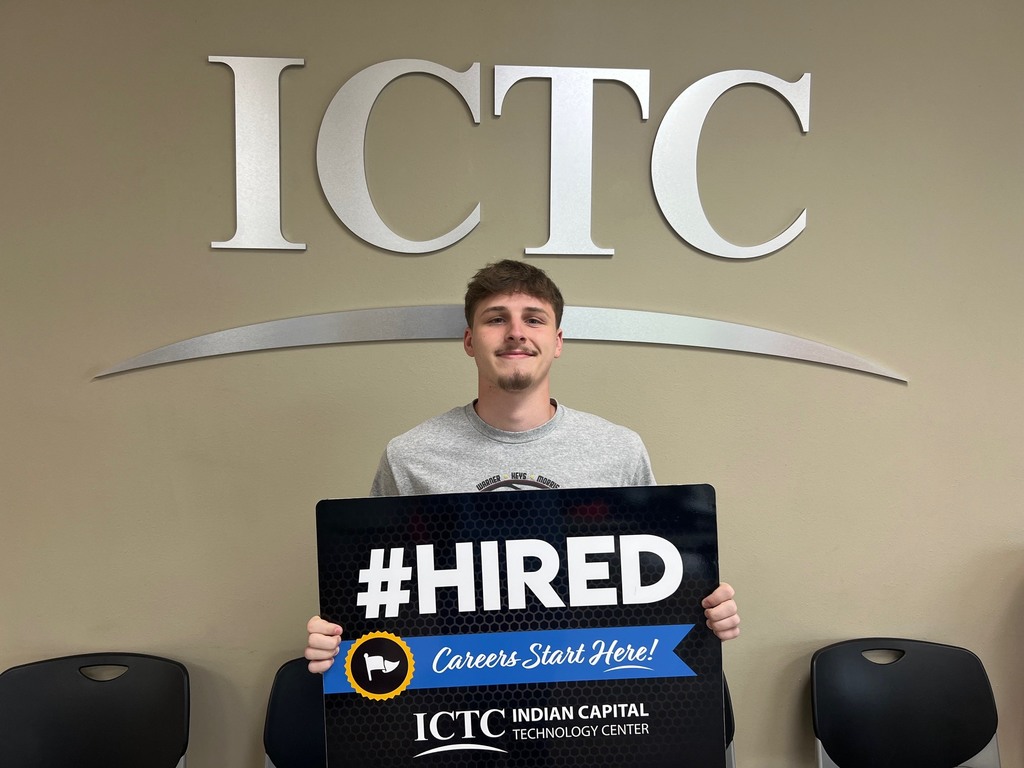 Man standing with a sign that reads "#HIRED" in front of a sign with the letters "ICTC."