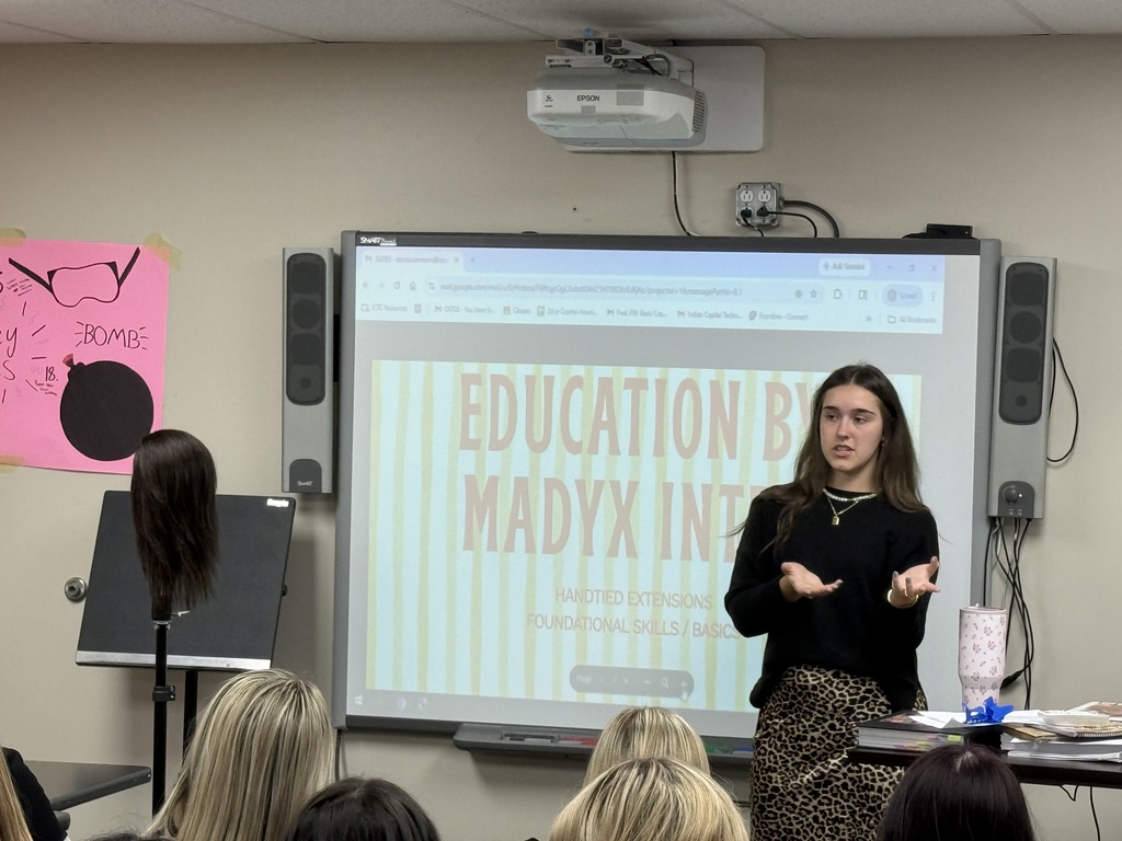 Woman stands before screen reading Education by Madyx Interactive. Audience of women sit in chairs before her.