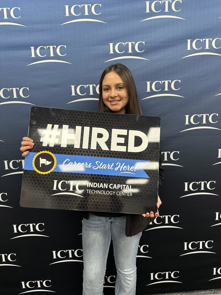 A woman in jeans holds a sign that reads "#HIRED" and "Careers Start Here" in front of a blue backdrop.