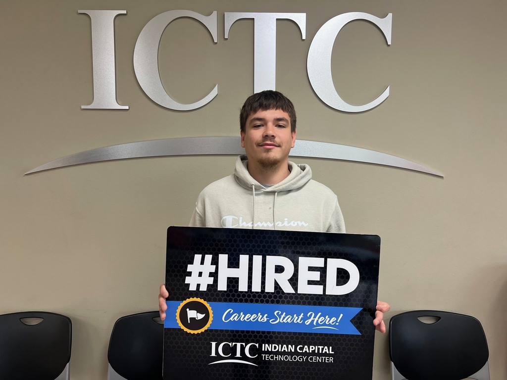 A young man in a white hoodie holds a sign reading "#HIRED" in front of an ICTC logo.
