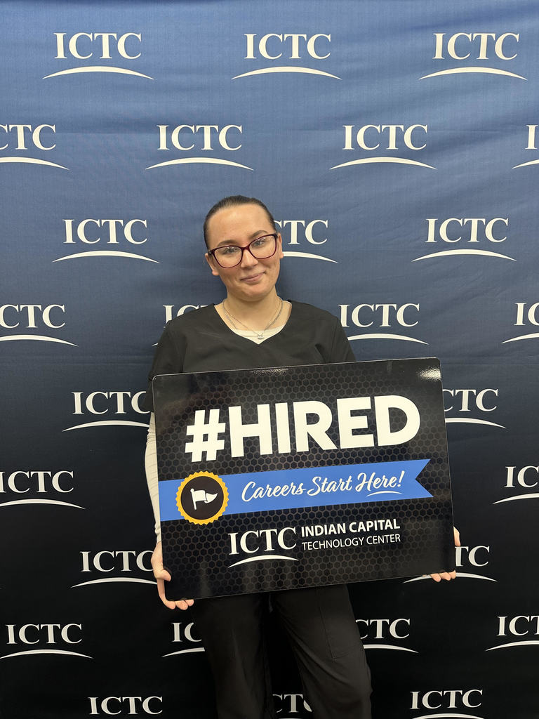 Person holding a sign that says "#HIRED Careers Start Here!" in front of a blue backdrop with text.