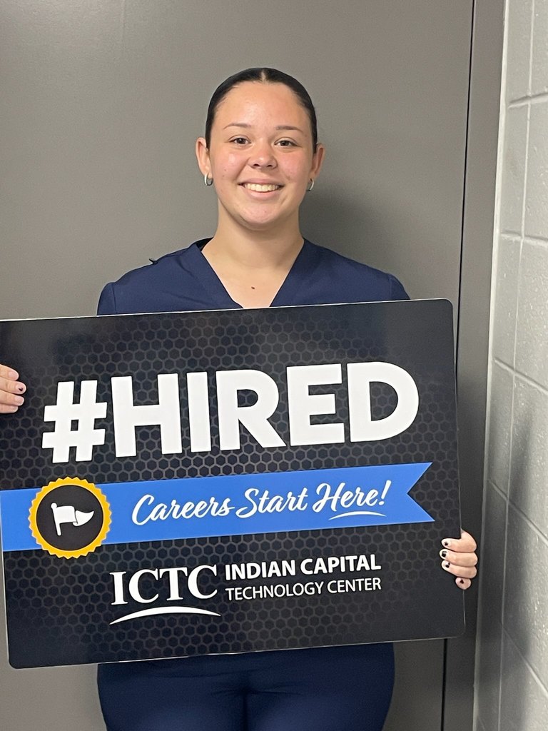 A woman in a blue uniform holds a sign reading "#HIRED Careers Start Here!" at Indian Capital Technology Center.