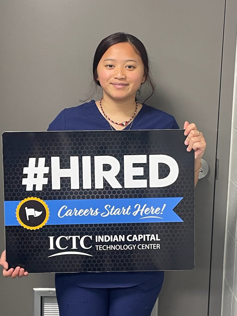 A woman in blue scrubs holds a sign that reads "#HIRED Careers Start Here!" with the ICTC logo on it.