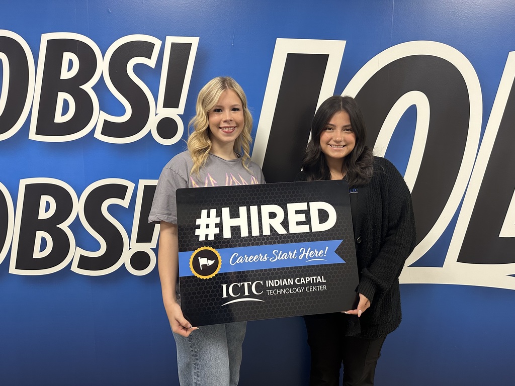 Two women stand before a wall with a large, blue background reading "OBS! 101" and holding a sign that says "#HIRED".