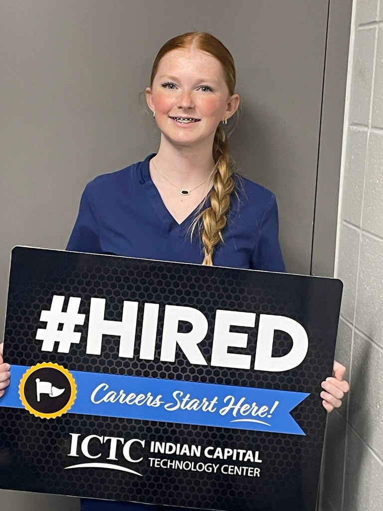 A person in a blue shirt holds a black sign saying "#HIRED" and "Careers Start Here!" against a gray background.