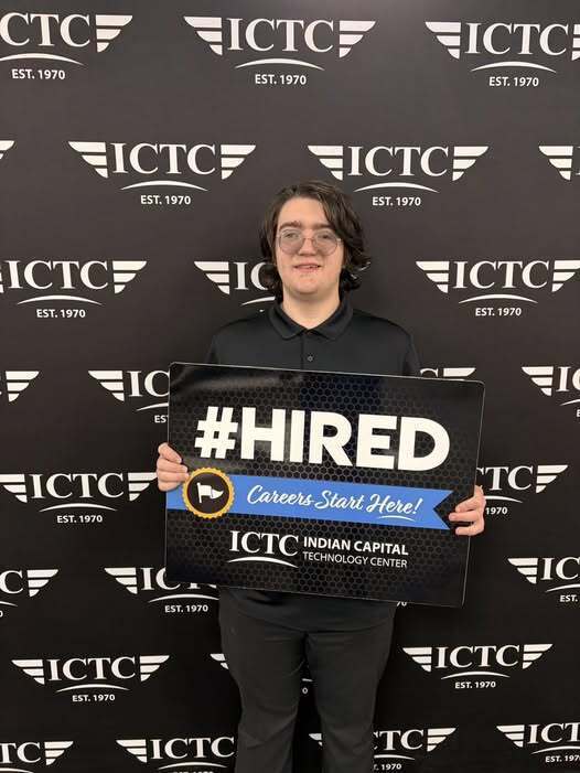 A person holding a black sign that says "#HIRED" with "Careers Start Here!" in front of a black backdrop with white text.