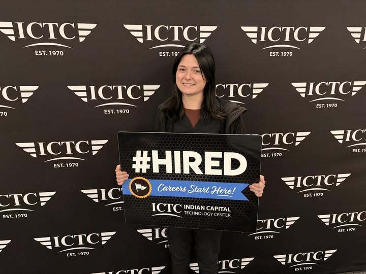 Person holding a sign that says "#HIRED" standing in front of a wall with multiple logos.