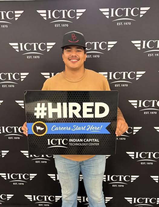 A man holds a sign reading "#HIRED" and smiles in front of a black backdrop with white text.