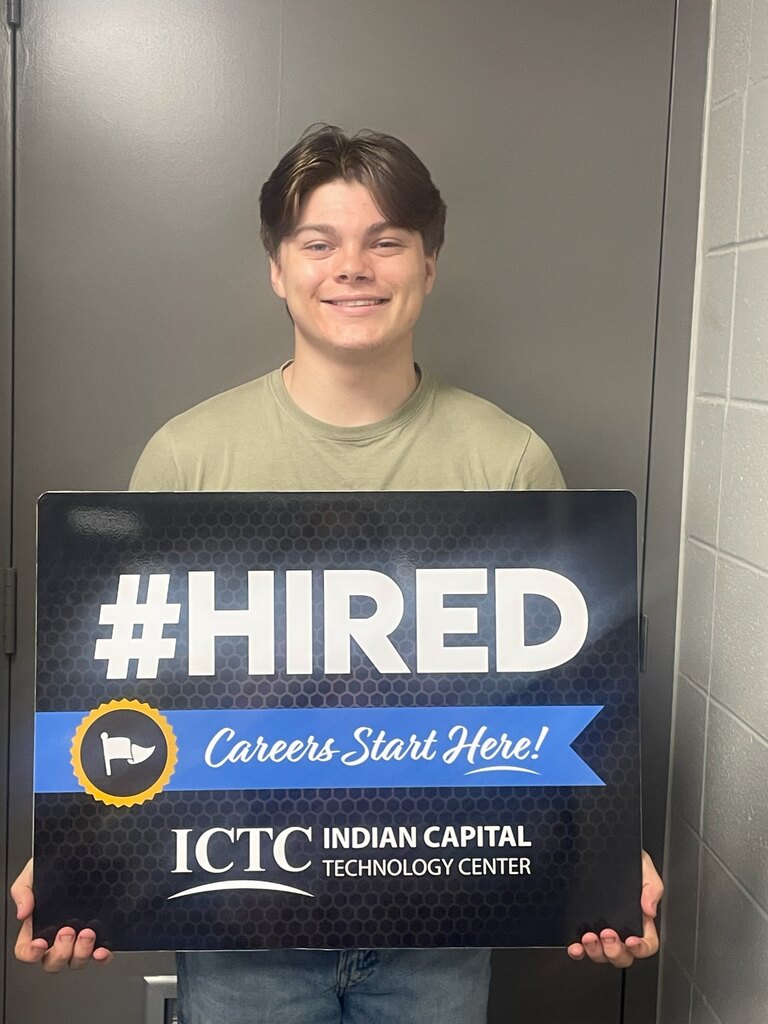 A man smiling and holding a sign that says "#HIRED Careers Start Here!" with a blue ribbon.