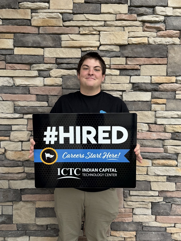Person holds sign reading "#HIRED" and "Careers Start Here!" in front of brick wall.