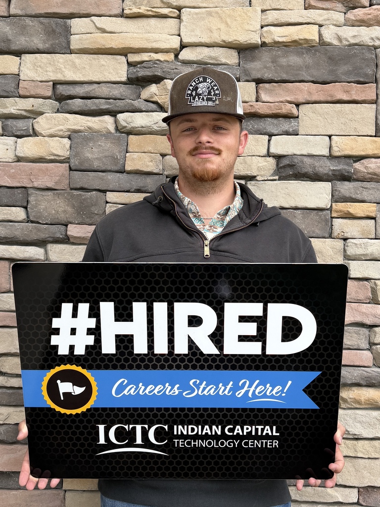 Man holds a black sign with white text reading "HIRED Careers Start Here!" in front of a stone wall.