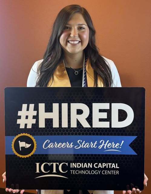 Woman in a white jacket and yellow stole holding a sign that says "#HIRED Careers Start Here!" for the Indian Capital Technology Center.