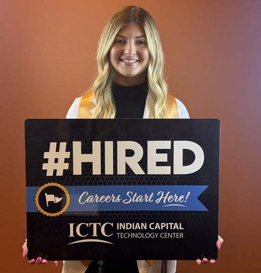 A woman holds a black sign with "#HIRED" and "Careers Start Here!" in front of her.
