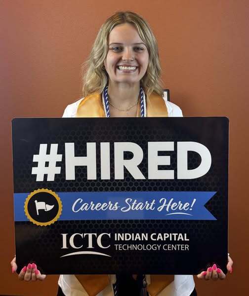 A woman in a cap and gown holds a sign saying "#HIRED Careers Start Here!" with blue and orange colors.