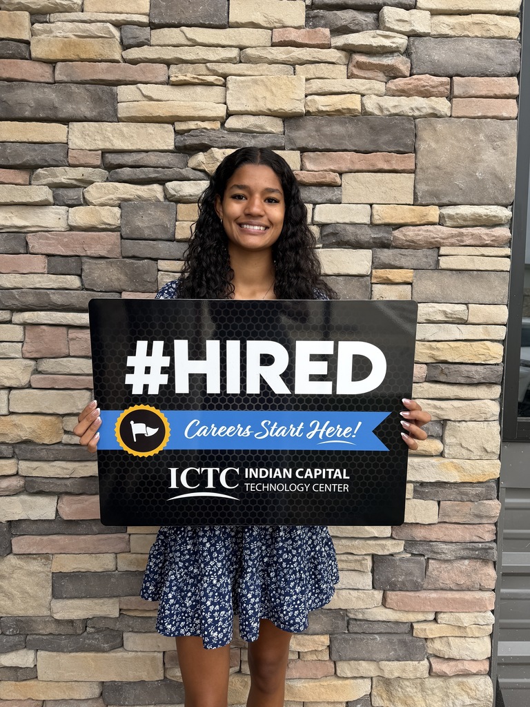 Woman standing in front of a brick wall, holding a sign with "#HIRED" and "Careers Start Here!" text.
