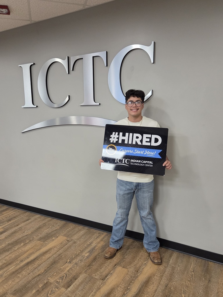 Person holding a sign that says "#HIRED" in front of the "ICTC" logo on a gray wall.