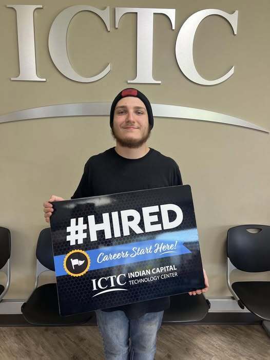 Man holding a sign that says "#HIRED" in front of a sign that says "ICTC".