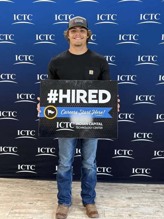 Person holding a sign that says #HIRED with a blue background. The sign has the words "Career Start Here!"
