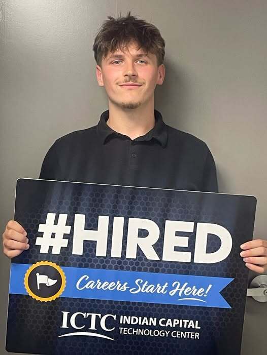 Man holding a sign that reads "#HIRED" and "Careers Start Here!" in front of a gray background.