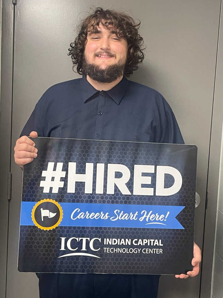 A man holds a sign saying "#HIRED" and "Careers Start Here!" from the Indian Capital Technology Center.