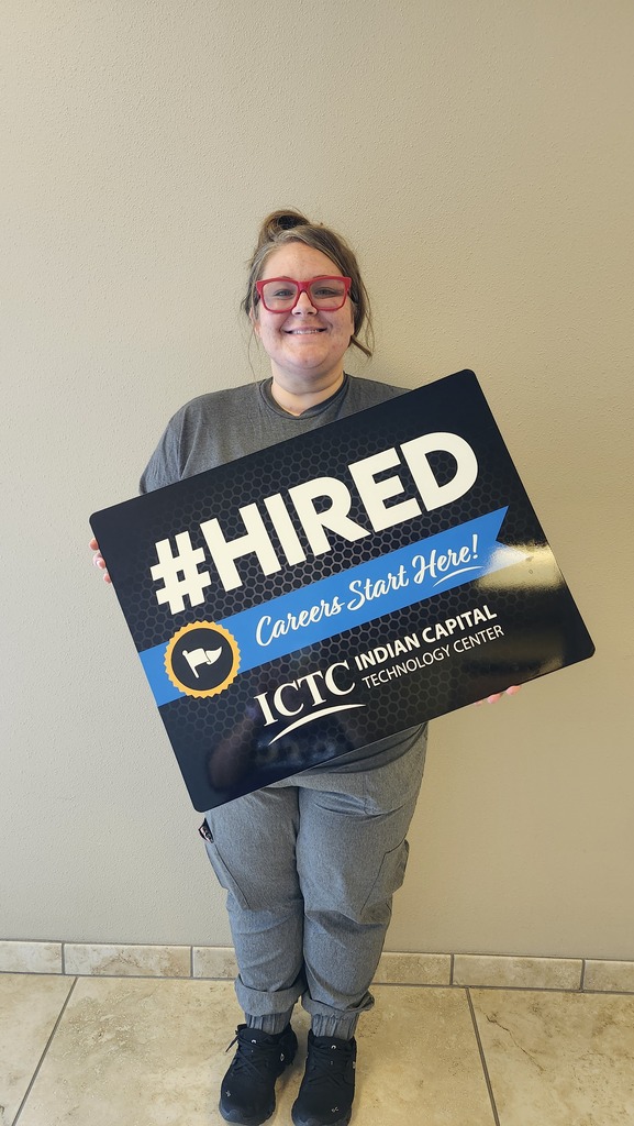 Person holding a black sign with white text "#HIRED" and "Careers Start Here!" standing in front of a light wall.