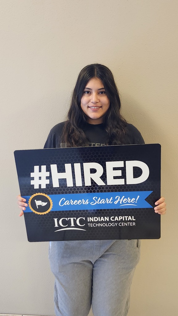 Woman holds a sign that says "#HIRED Careers Start Here!" in front of a plain wall.