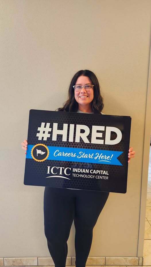 Person holds a black sign with white letters and a blue logo. The sign says "#HIRED" and "Careers Start Here!".