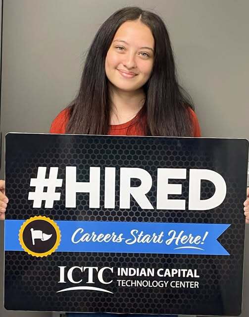 A woman with long hair smiles, holding a rectangular sign that says "#HIRED" and "Careers Start Here!" with a logo for ICTC.