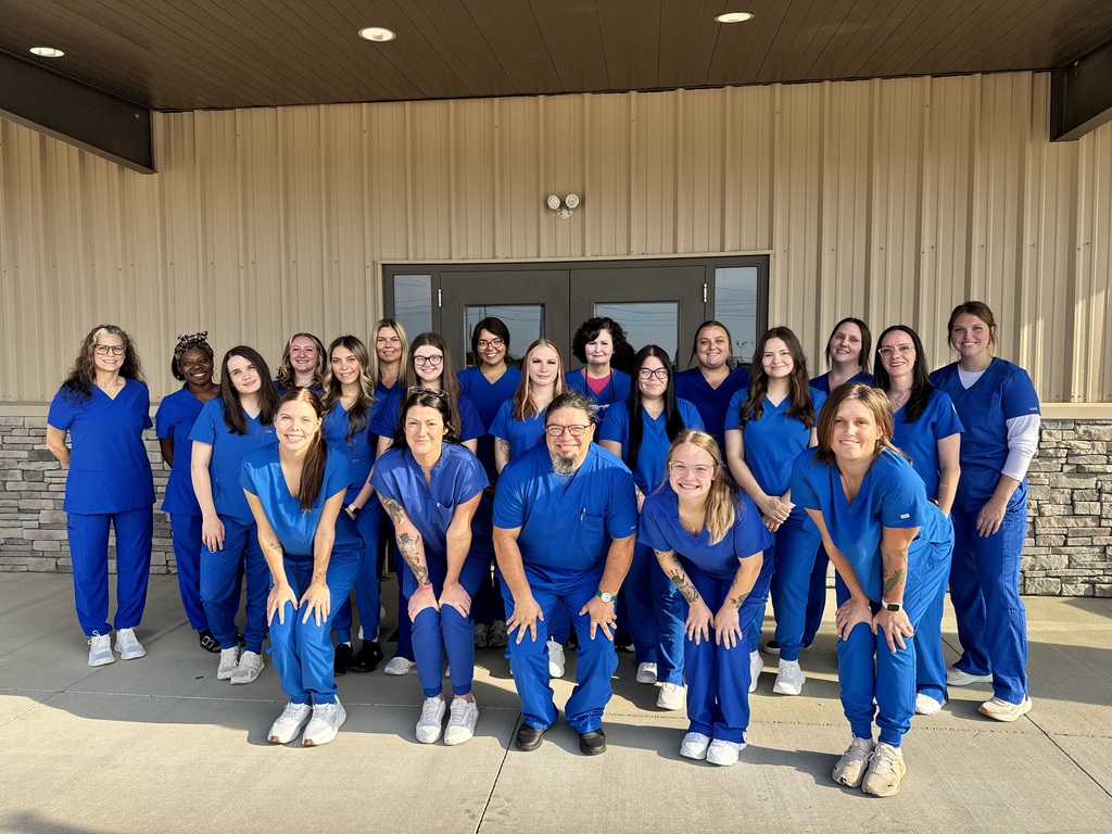 A group of medical staff in blue scrubs stands together in front of a building.
