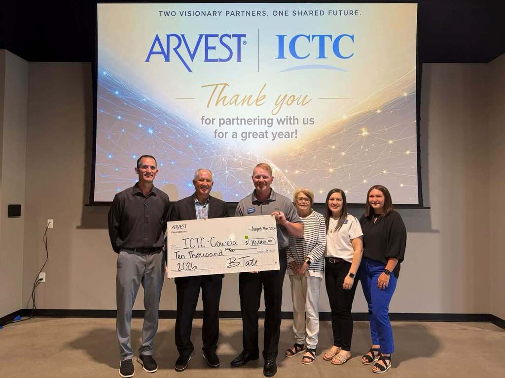 Five people in formal attire stand next to a large check. Behind them, a projector screen displays "ARVEST ICTC Thank you for partnering with us for a great year."