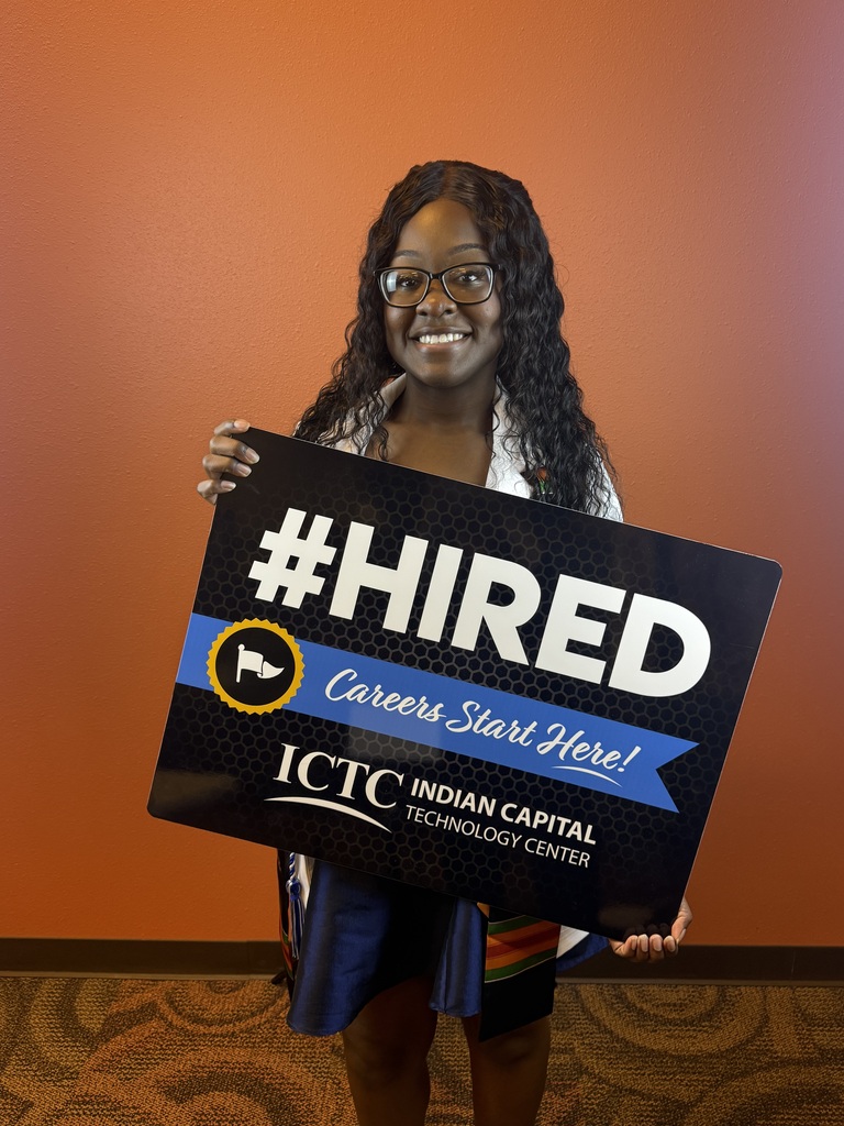 Person holds a black placard with white text reading "#HIRED" in front of an orange wall.