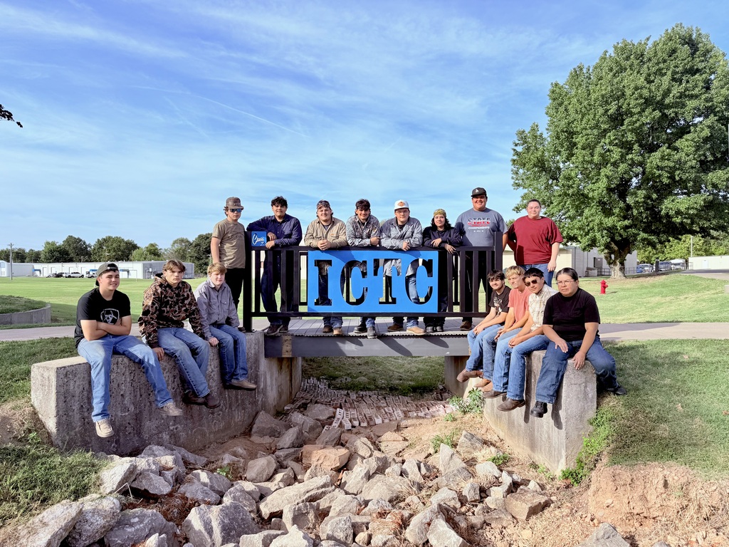 A group of people pose for a photo in front of a sign that reads "ICTC" on a bridge over rocks.