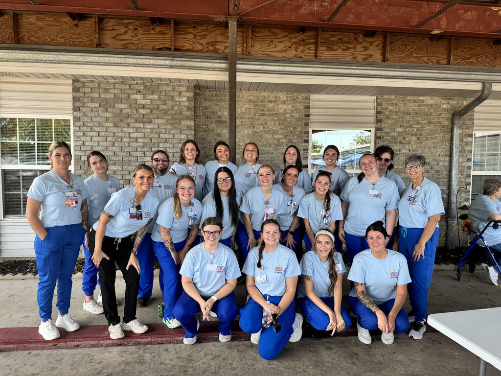 A group of people in blue scrubs and white shoes pose for a photo outside a brick building.
