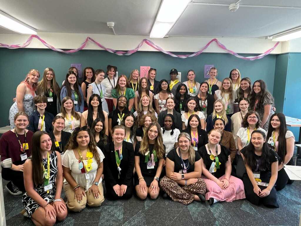 A large group of people in a room, wearing name tags, posing for a photo with colorful decorations on the wall.