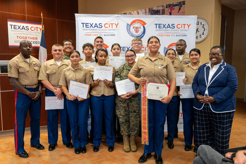TCHS Marine Corps JROTC students pose with certificates in front of a TCISD backdrop.