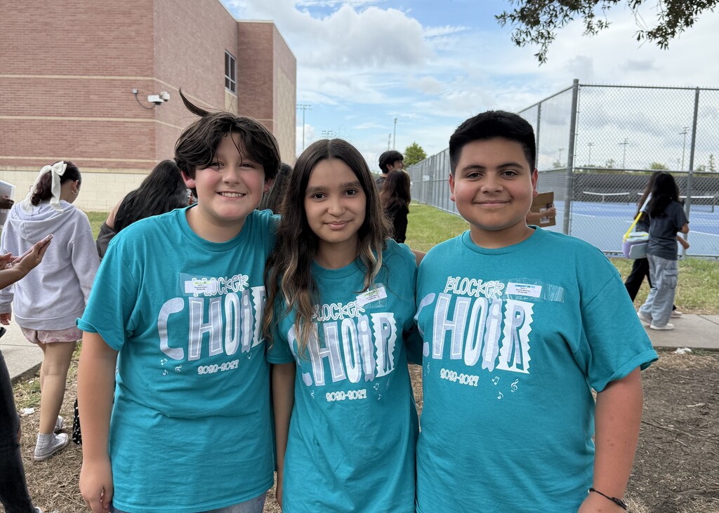 Three students pose together wearing teal Blocker choir T-shirts while smiling