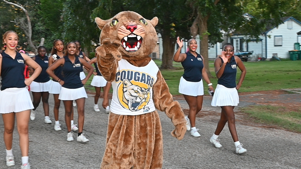 The LMHS Cougar mascot is in the middle waving and is surrounding by cheerleaders in the Homecoming parade