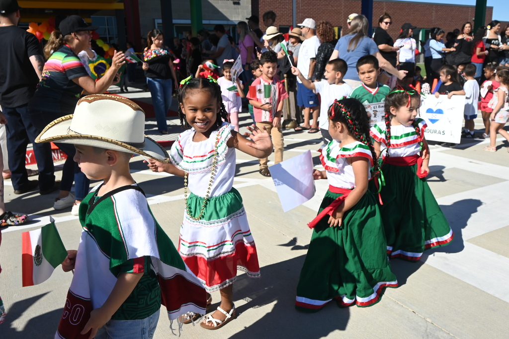 Students dressed in traditional red, green and white dancer dresses while some hold flags from Mexico