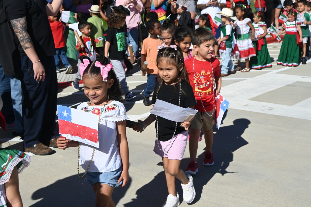 Students walking single file holding their handmade flags from Chile and also wearing plastic metallic beads