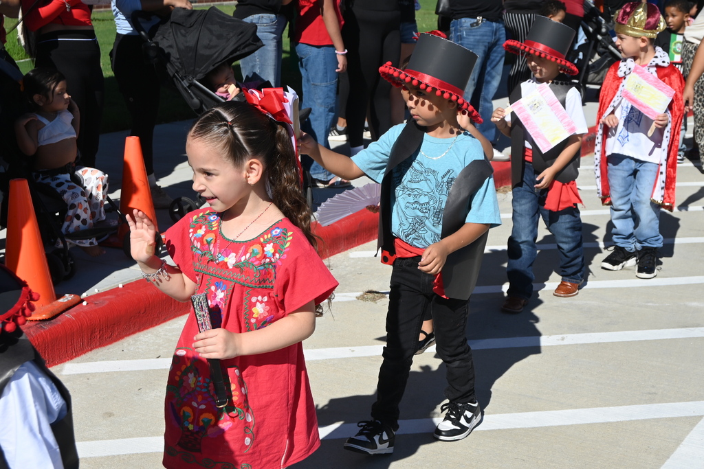 Students wear colorful clothing like black vests and red sashes and traditional black hats with red trim to represent Spain.