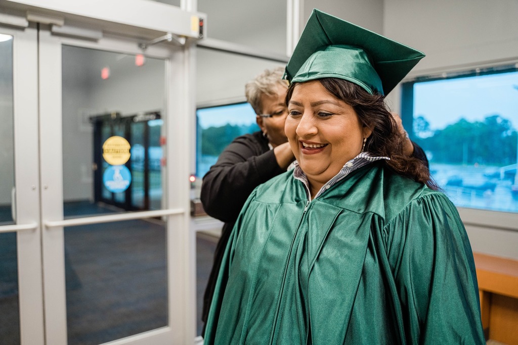 adult student wearing graduation gown being helped by a staff member