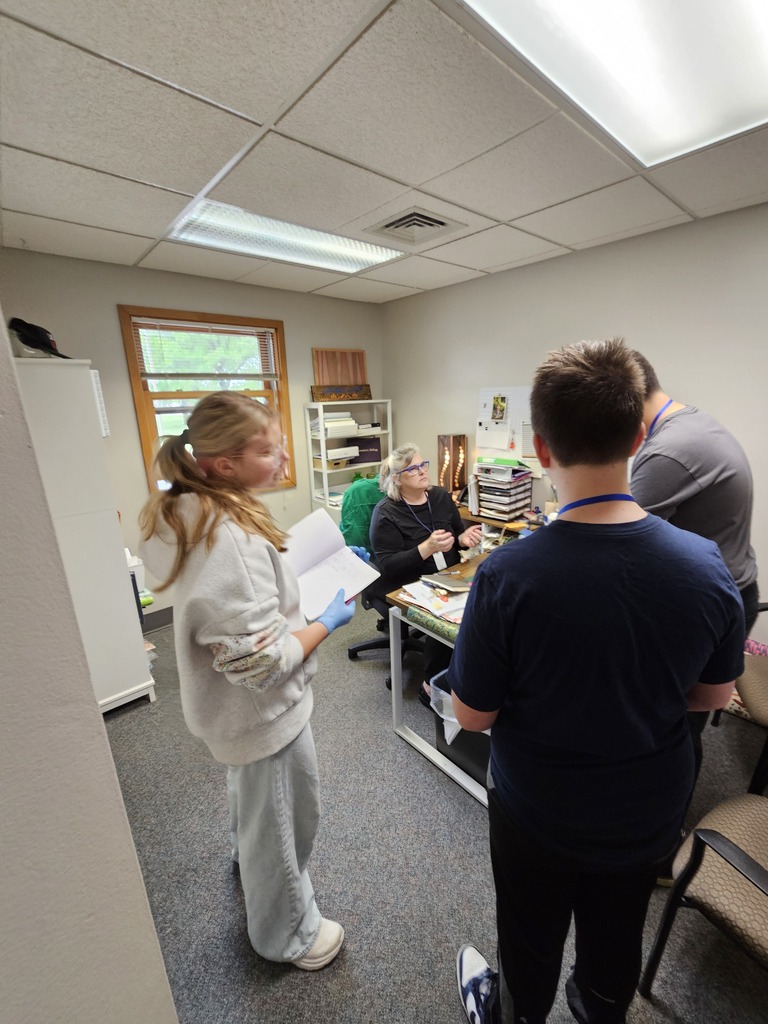 Junior High students gather in an office classroom space discussing clues and evidence with the Head of School during a collaborative forensic science investigation activity.